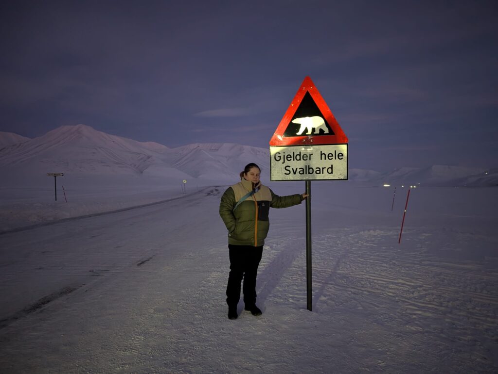 Winter clothing during Polar Night in Svalbard beside polar bear warning sign
